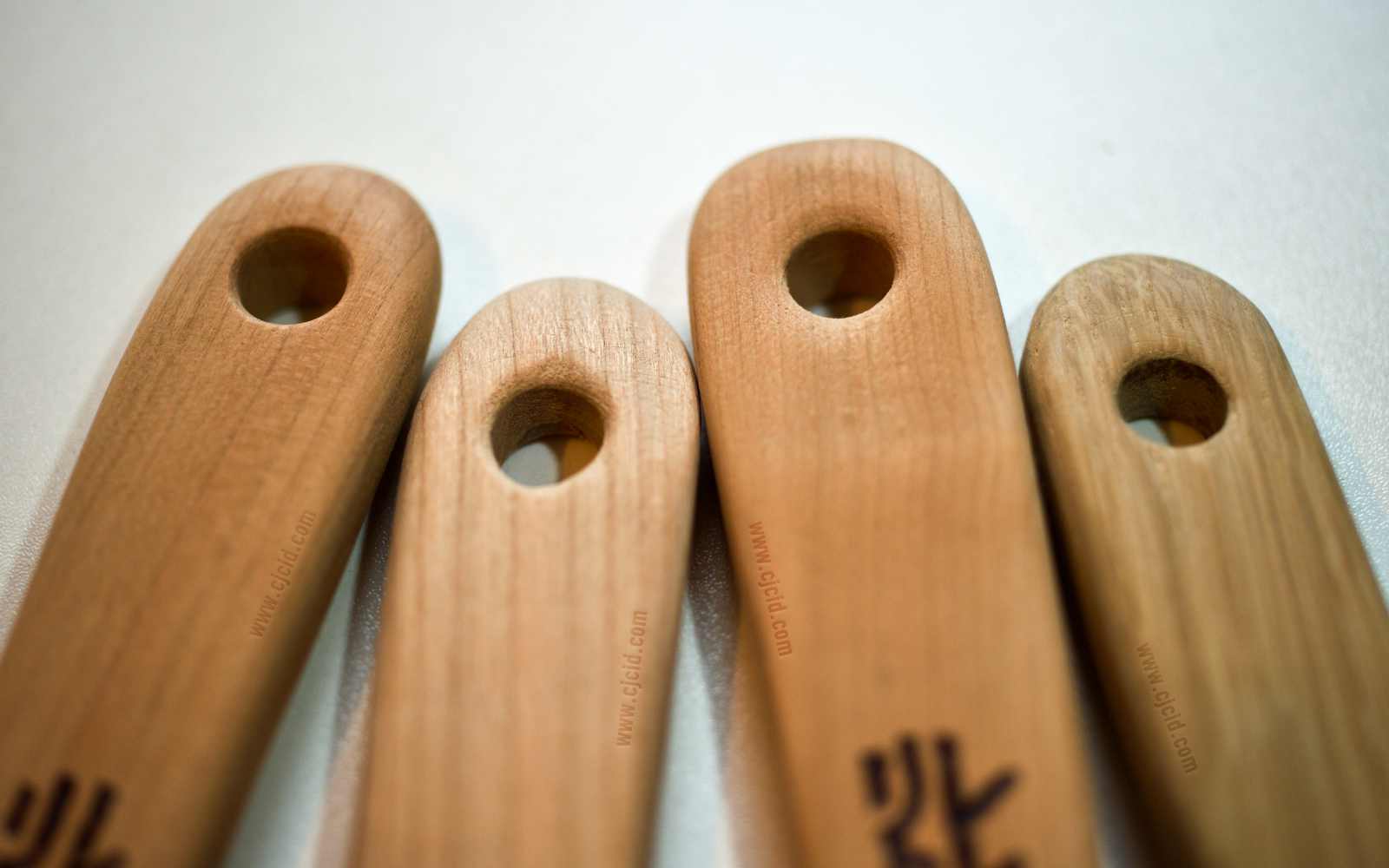 Close up on the neck’s hanging hole of four cooking spatulæ, made from single blocks of solid Sakura or Oak woods