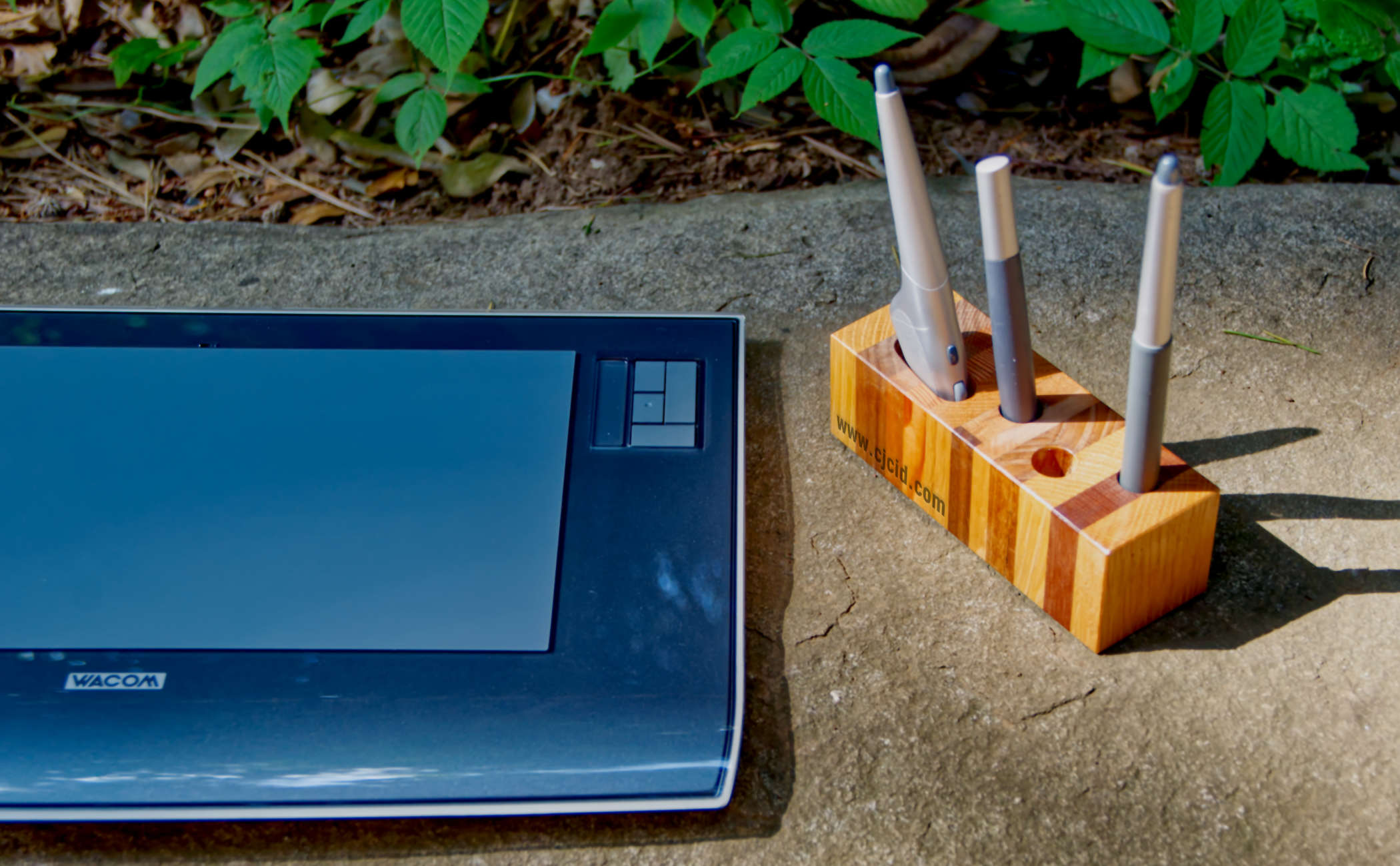 Top view of the handmade wooden pen holder “CJ Triplet Cuboid”, with 3 Wacom styluses in place, and a Wacom Intuos 3 next to it