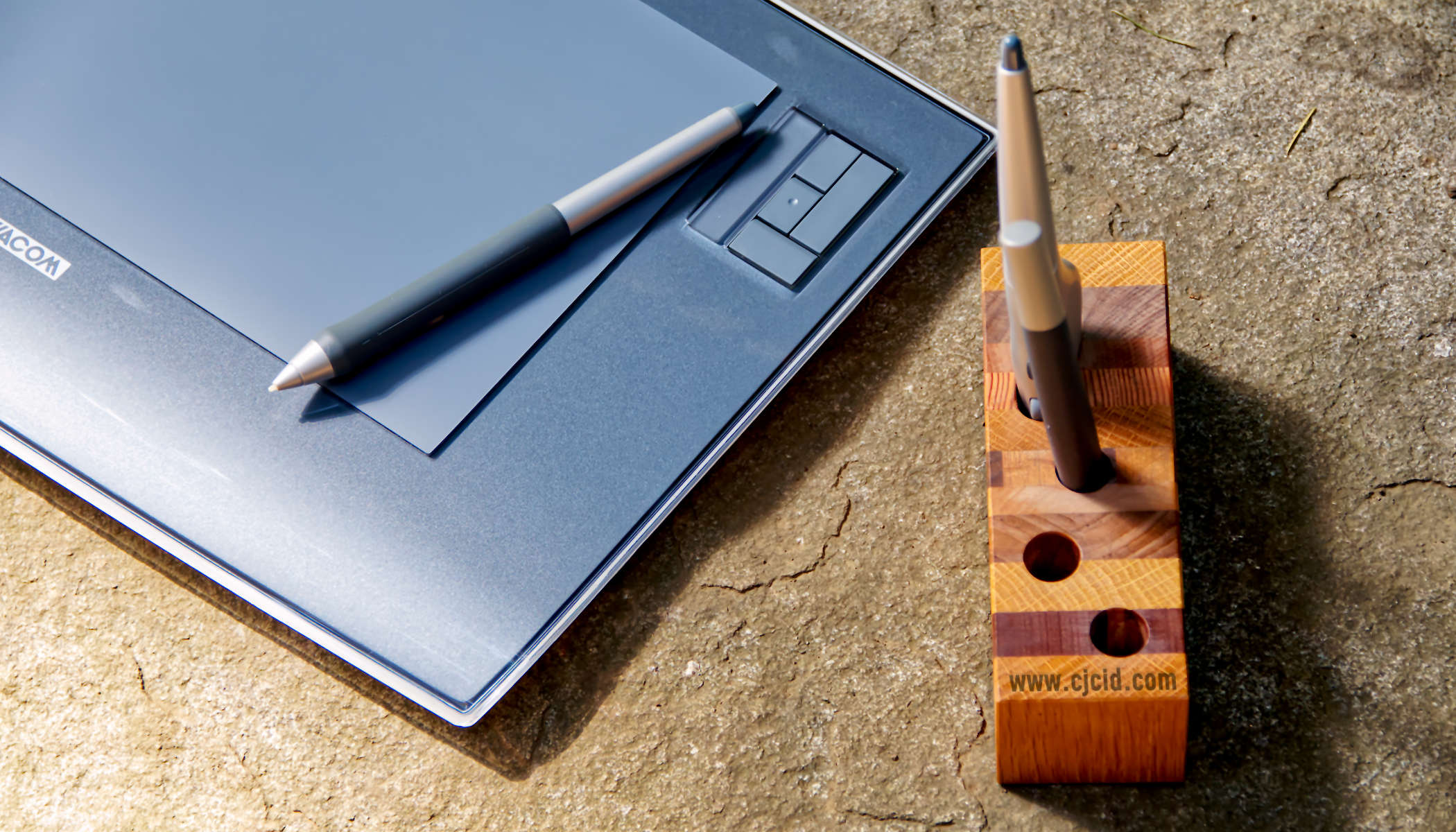 Top view of the handmade wooden pen holder “CJ Triplet Cuboid”, with 2 Wacom styluses in place, the Wacom Intuos 3 next to it, and the Wacom grip pen laying on the drawing tablet